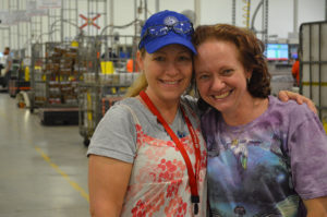 Two women in a factory hugging one another.