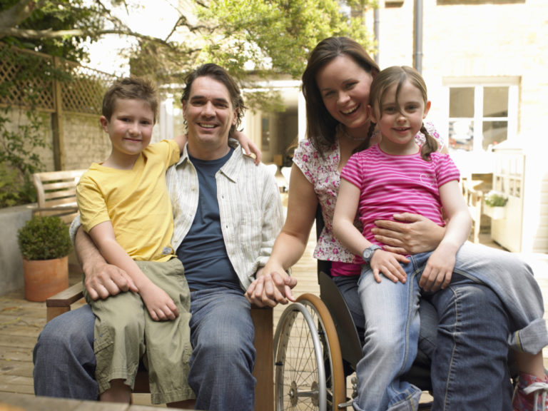 Family sitting in garden, woman in wheelchair, smiling, portrait
