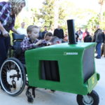 Young boy in wheelchair sits in custom tractor costume.