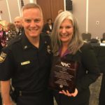 Angie McKinley holding an award next to a police officer