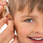 A boy smiles as someone places a hearing aid on his ear.