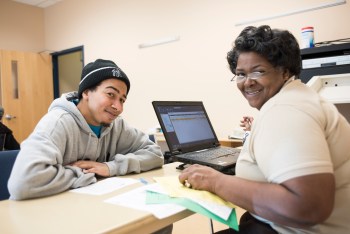 Two people working on taxes turn to the camera and smile