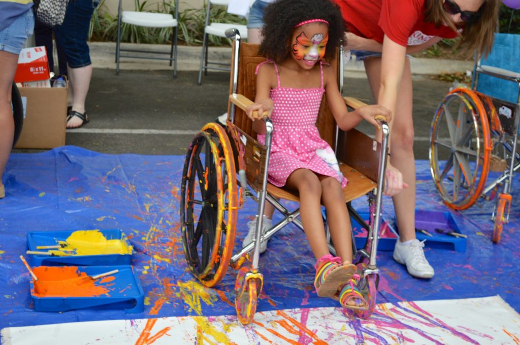 A child lifts her feet to get ready to roll across the canvas in a wheelchair.