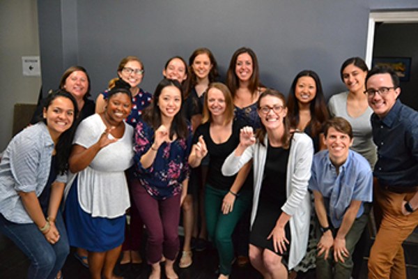 A group of individuals smile for a picture. Four people spell out “CORE” using sign language.