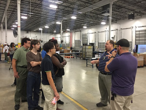 Two men talk with a group of young people on the floor of a large warehouse.