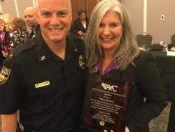 Angie McKinley holding an award next to a police officer