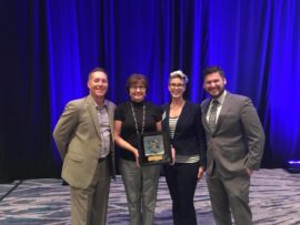 Four people smiling for a photo. One person is being presented an award.